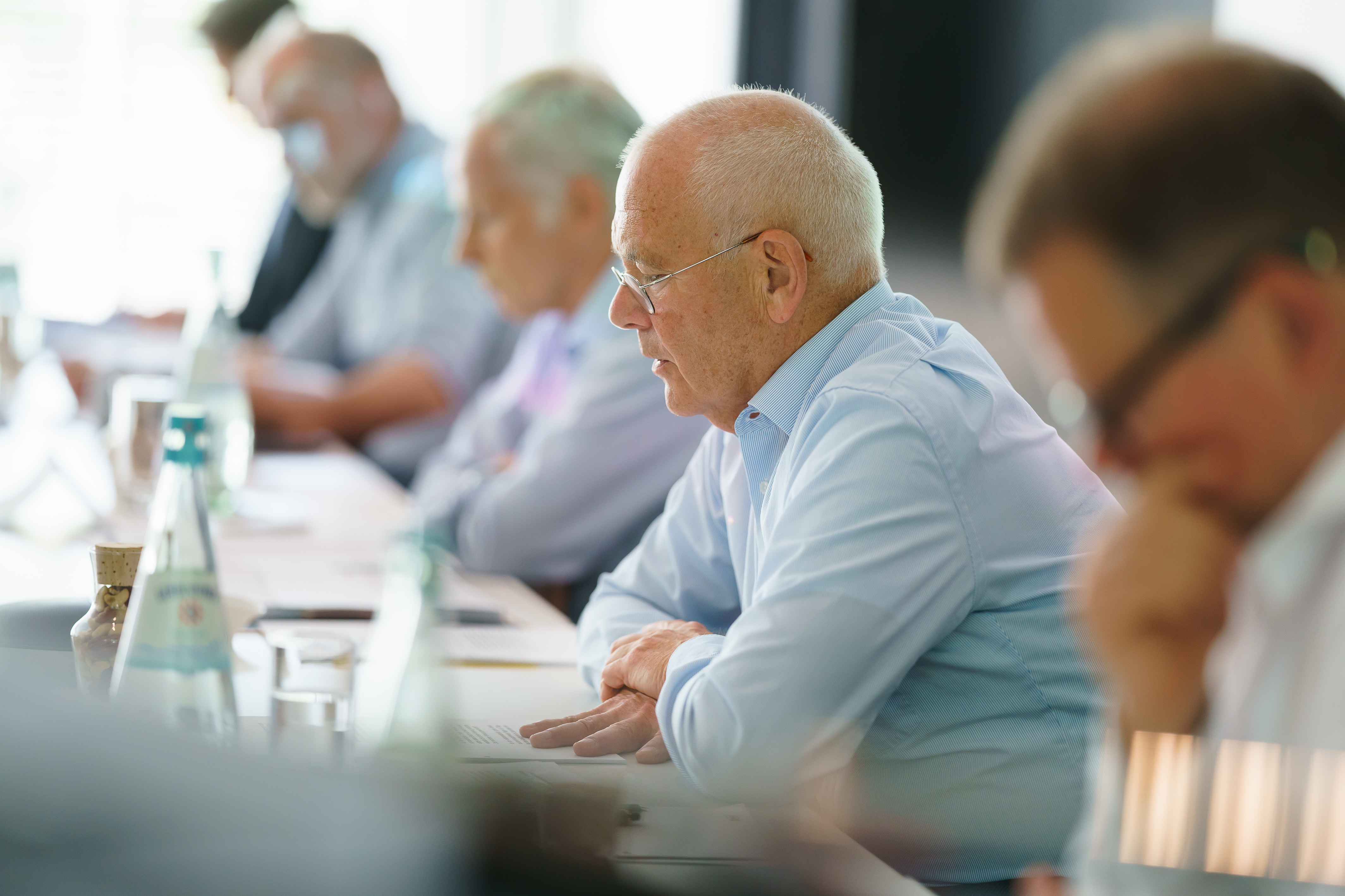 Älterer Mann in Brille spricht bei Konferenztisch mit Kollegen