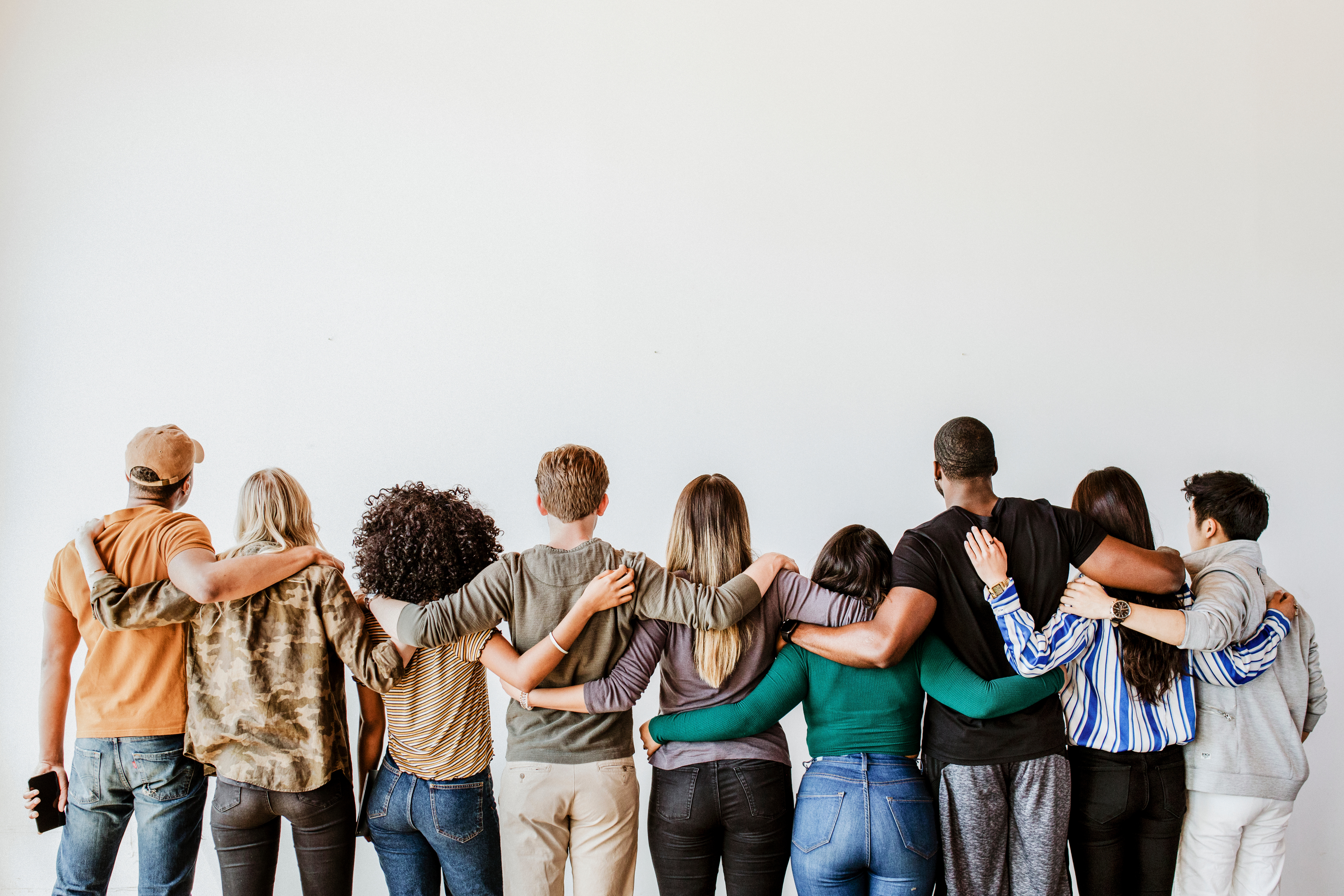 Diverse Gruppe von Menschen umarmt sich von hinten gegen helle Wand
